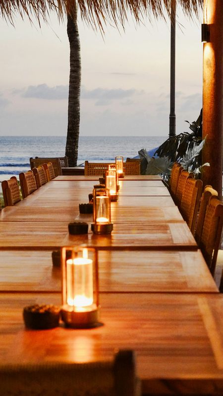 Mesa de madera frente al mar con faroles encendidos a la hora del atardecer