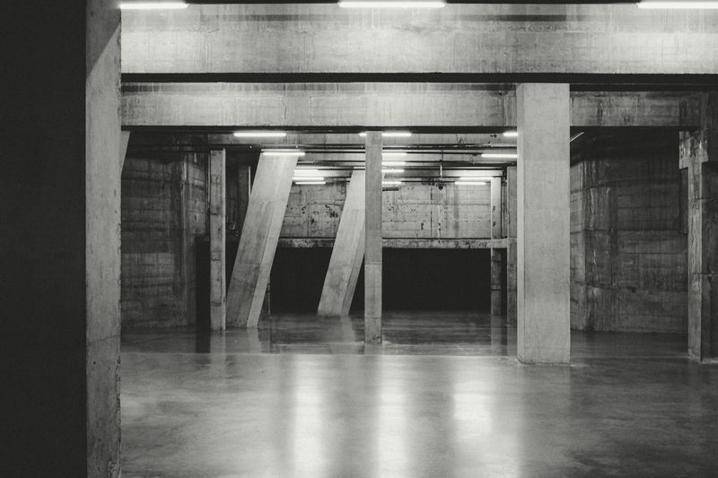 Sala amplia de hormigón con pilares inclinados y tubos de luz, en blanco y negro
