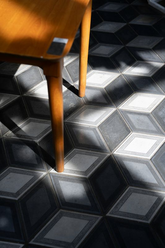 Pata de una silla de madera sobre baldosas en blanco y negro cruzadas por sombras