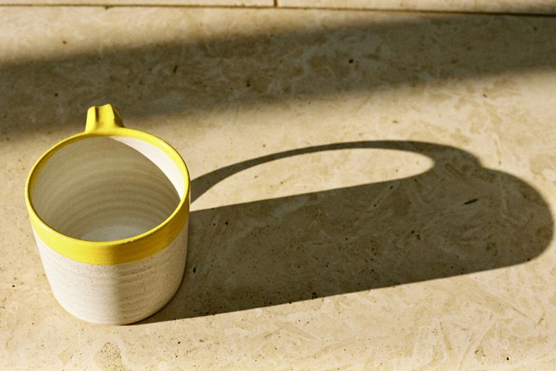 Taza blanca de borde amarillo con una larga sombra sobre una piedra clara