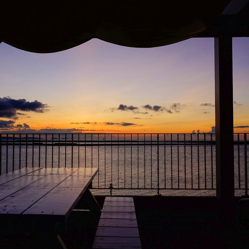 Mesa y baranda de una terraza frente al mar con el cielo violeta y naranja al fondo