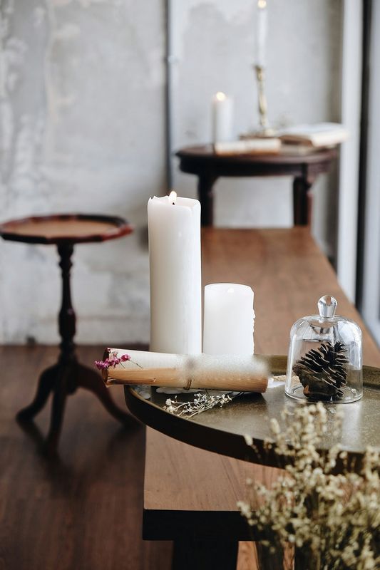 Velas blancas sobre una mesa de madera, con una campana de vidrio y una piña seca