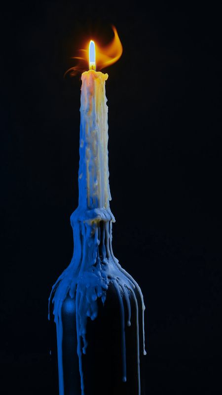 Vela encendida sobre una botella oscura, con la cera azul escurriendo por el vidrio