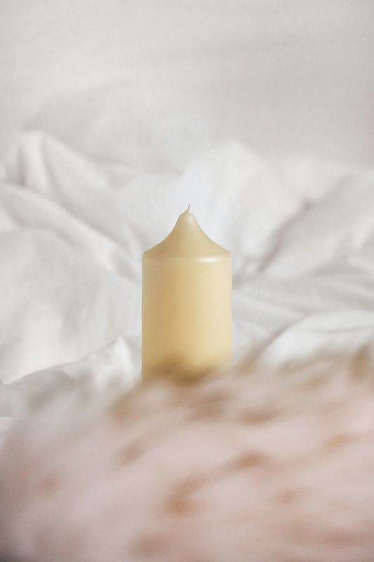 Vela crema sobre sábanas blancas arrugadas
