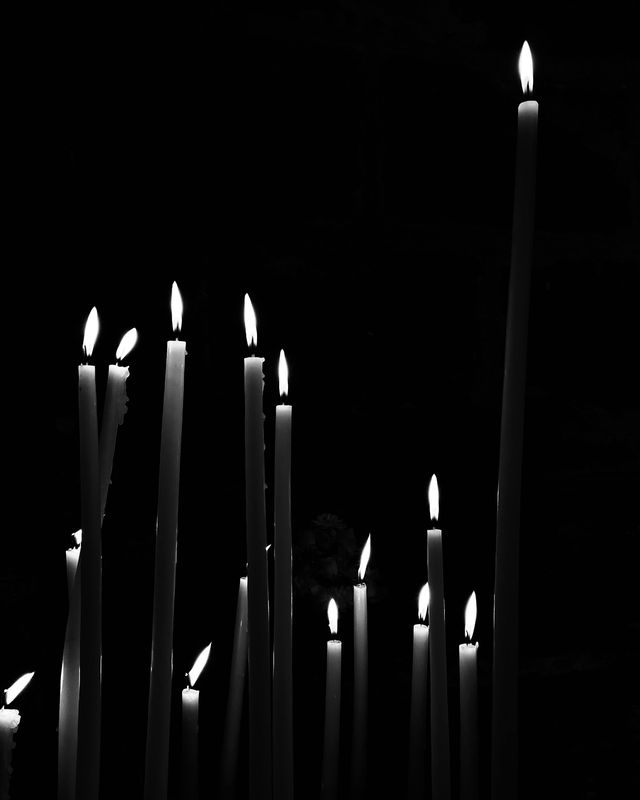Velas largas y delgadas encendidas en la oscuridad, en blanco y negro