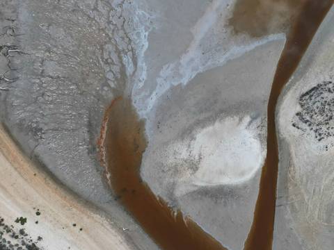 Cauce pardo que atraviesa una cuenca de sal gris y rosada, vista aérea