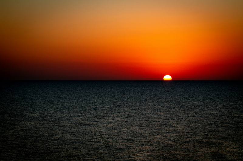 Sol rojo sobre el horizonte y un mar oscuro