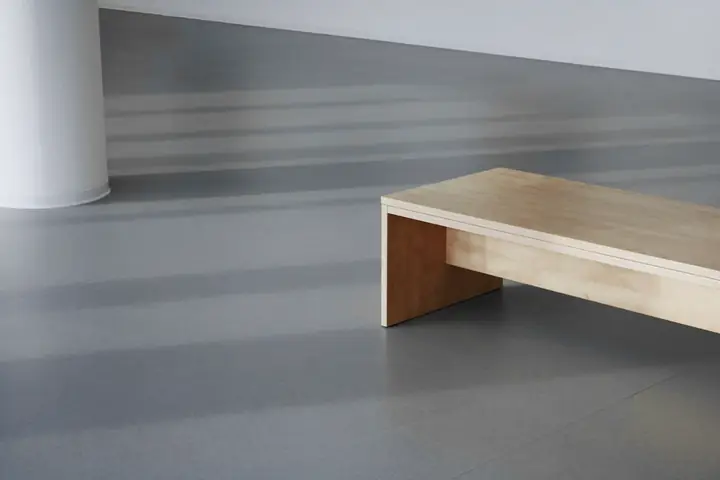 Banca baja de madera clara sobre un suelo gris azulado
