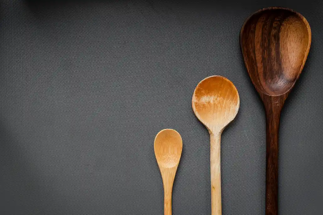 Tres cucharas de madera de distinto tamaño sobre un fondo gris