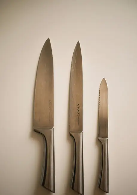 Tres cuchillos de cocina colgados en una pared clara