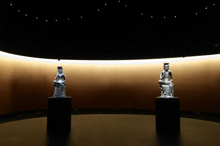 Dos piezas sobre peanas negras en una sala curva de luz cálida