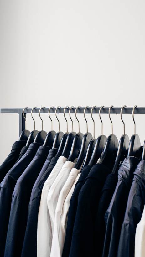 Camisas y chaquetas colgadas de una barra delante de una pared blanca