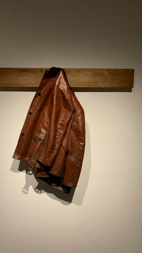 Chaqueta de cuero marrón colgada de un riel de madera