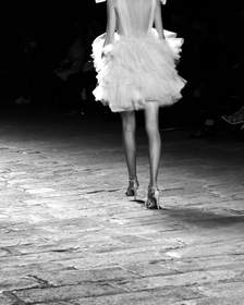 Figura de espaldas con falda de volantes en una pasarela, en blanco y negro