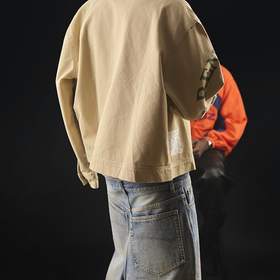Figura de espaldas con chaqueta crema sobre un escenario oscuro