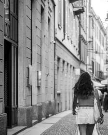 Figura de espaldas que camina por un callejón empedrado, en blanco y negro