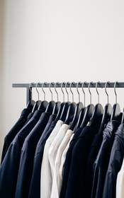 Camisas y chaquetas colgadas de una barra delante de una pared blanca