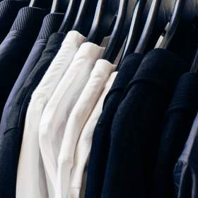 Camisas y chaquetas colgadas de una barra delante de una pared blanca