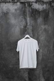 Camiseta blanca colgada de una percha sobre una pared de cemento