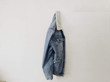 Chaqueta de mezclilla colgada de un clavo sobre una pared clara