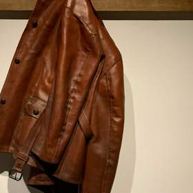 Chaqueta de cuero marrón colgada de un riel de madera