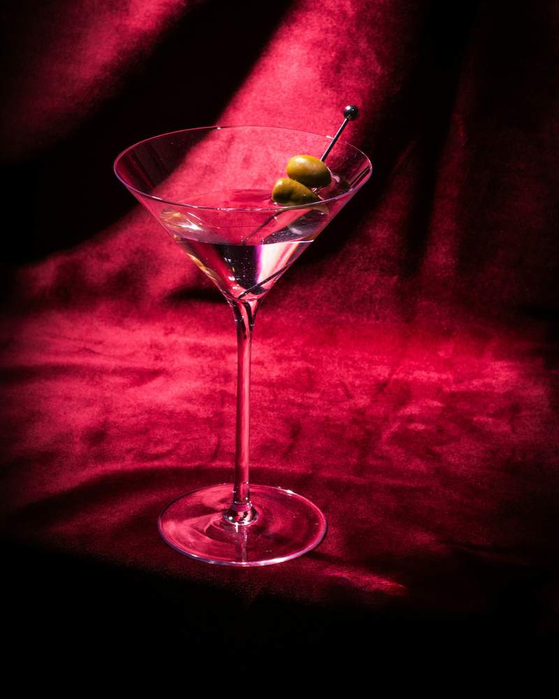 Copa de martini con aceitunas sobre una tela roja con luz dirigida