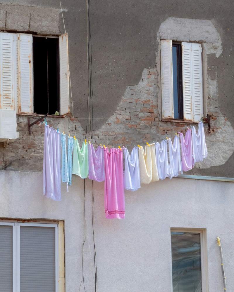 Ropa de colores pastel tendida entre dos ventanas de un muro antiguo