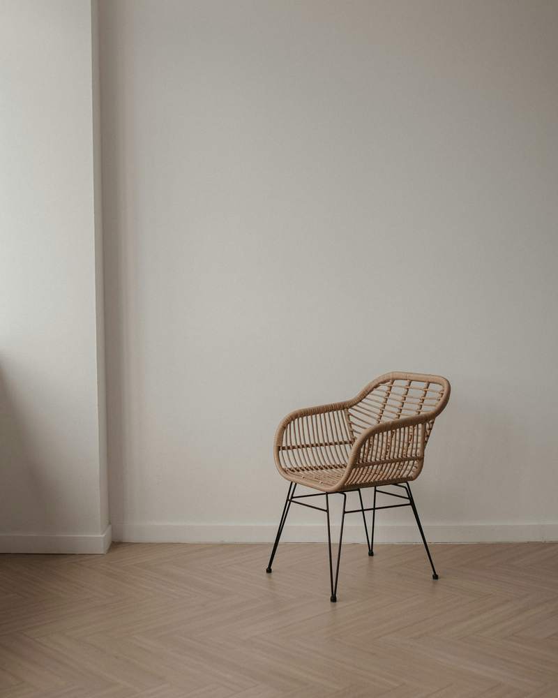Silla de ratán en una sala vacía con piso de parquet y luz suave