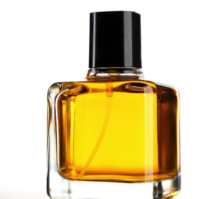 Frasco cuadrado de vidrio con perfume dorado y tapa negra, sobre fondo blanco