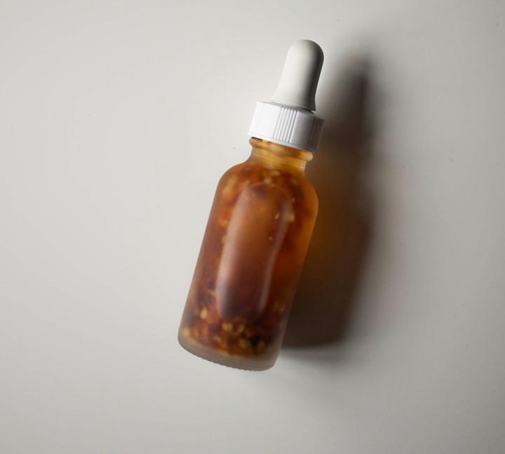 Frasco de vidrio ámbar con tapa blanca, apoyado sobre una pared gris