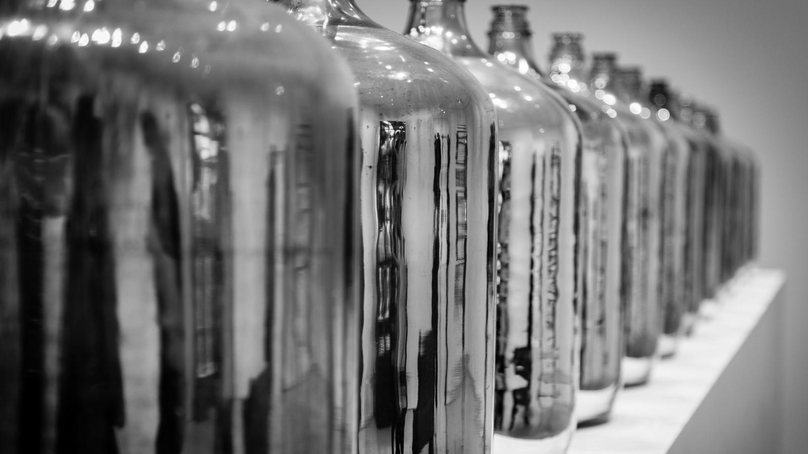 Fila de grandes damajuanas de vidrio en blanco y negro, que se pierde hacia el fondo