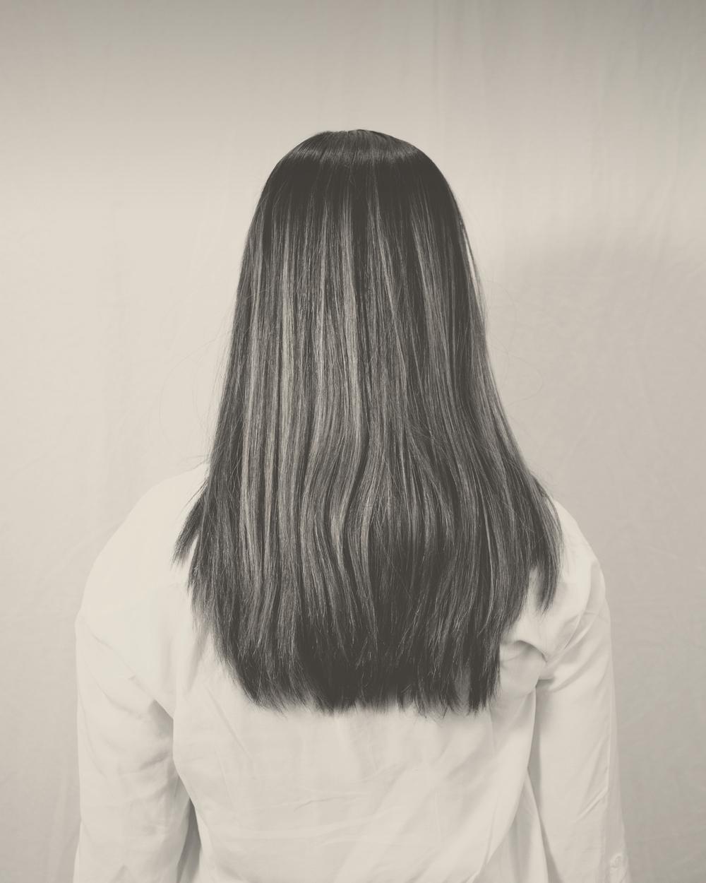 Una mujer de espaldas con el pelo liso y largo y una camisa blanca, en blanco y negro cálido