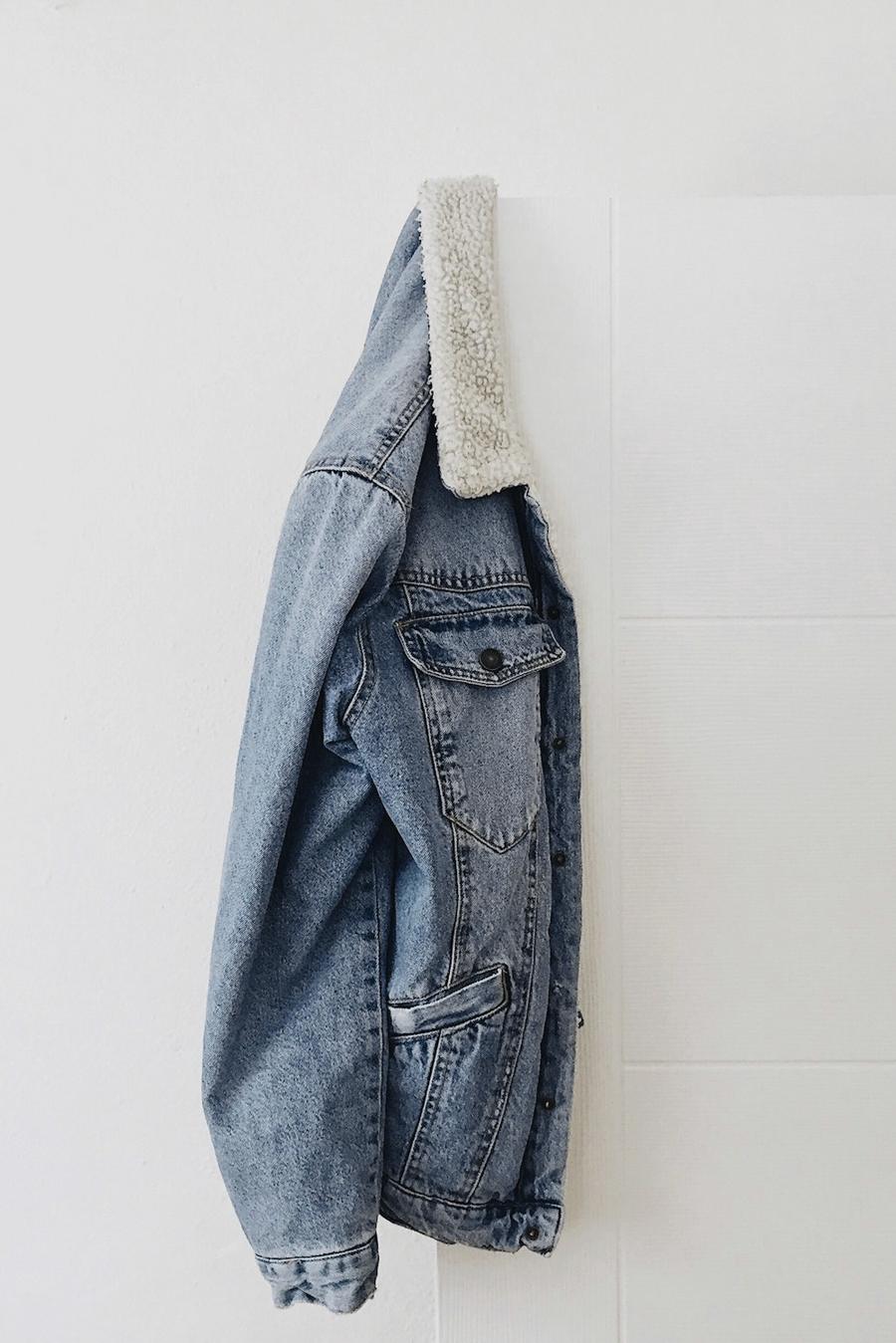 Una chaqueta de mezclilla clara con cuello de borrego colgada en una pared blanca