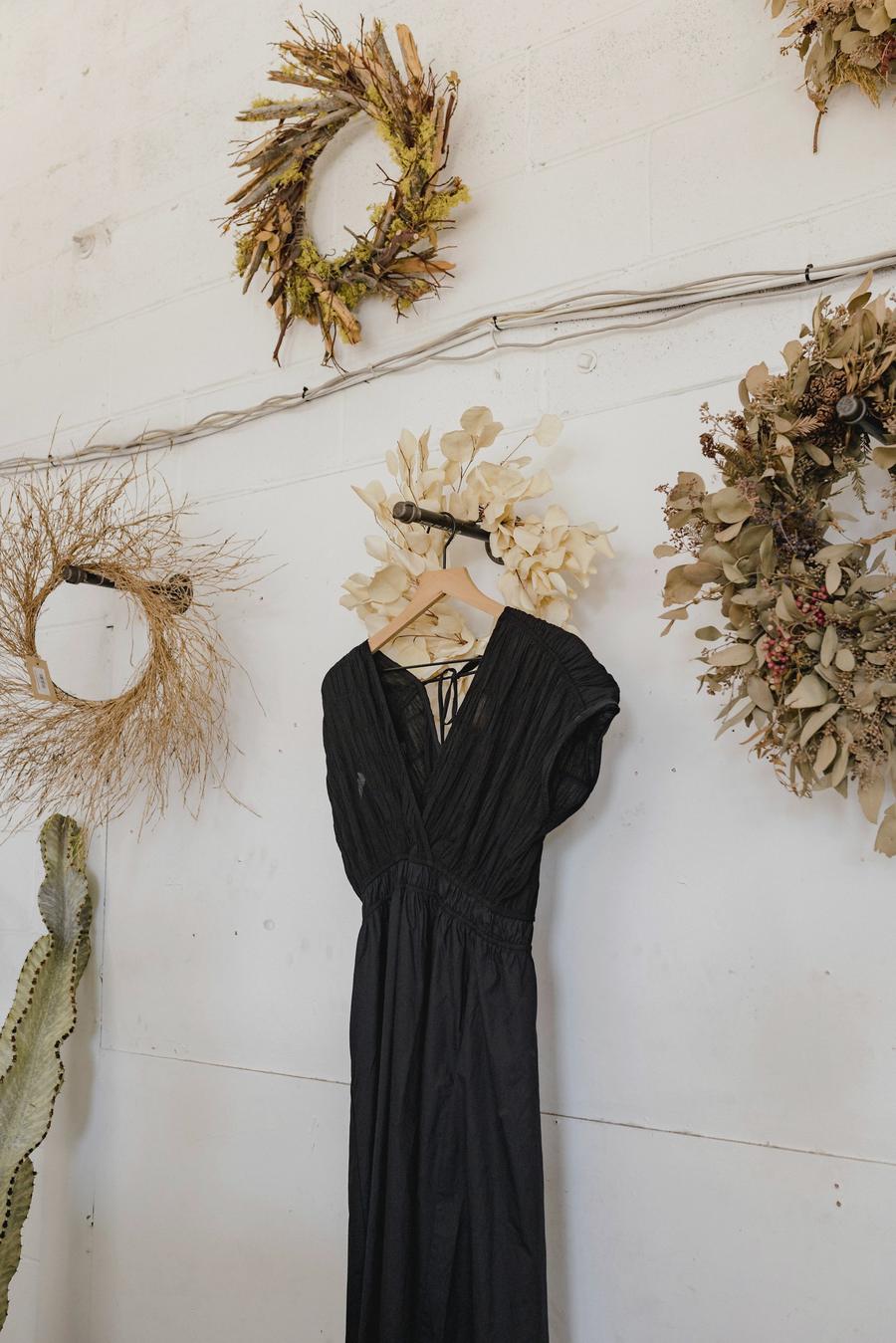 Un vestido negro de gasa colgado en una pared blanca entre coronas de flores secas