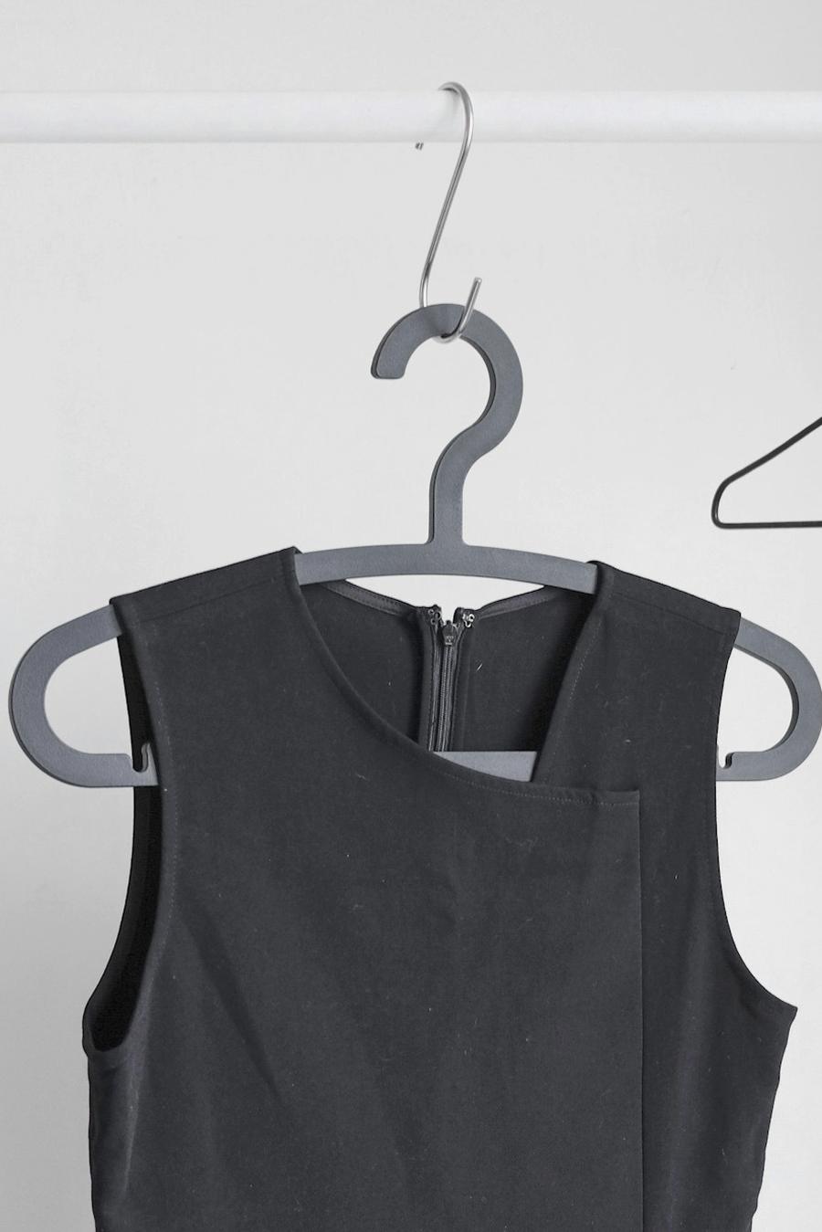 Un vestido gris oscuro sin mangas colgado de una percha de plástico gris frente a una pared clara