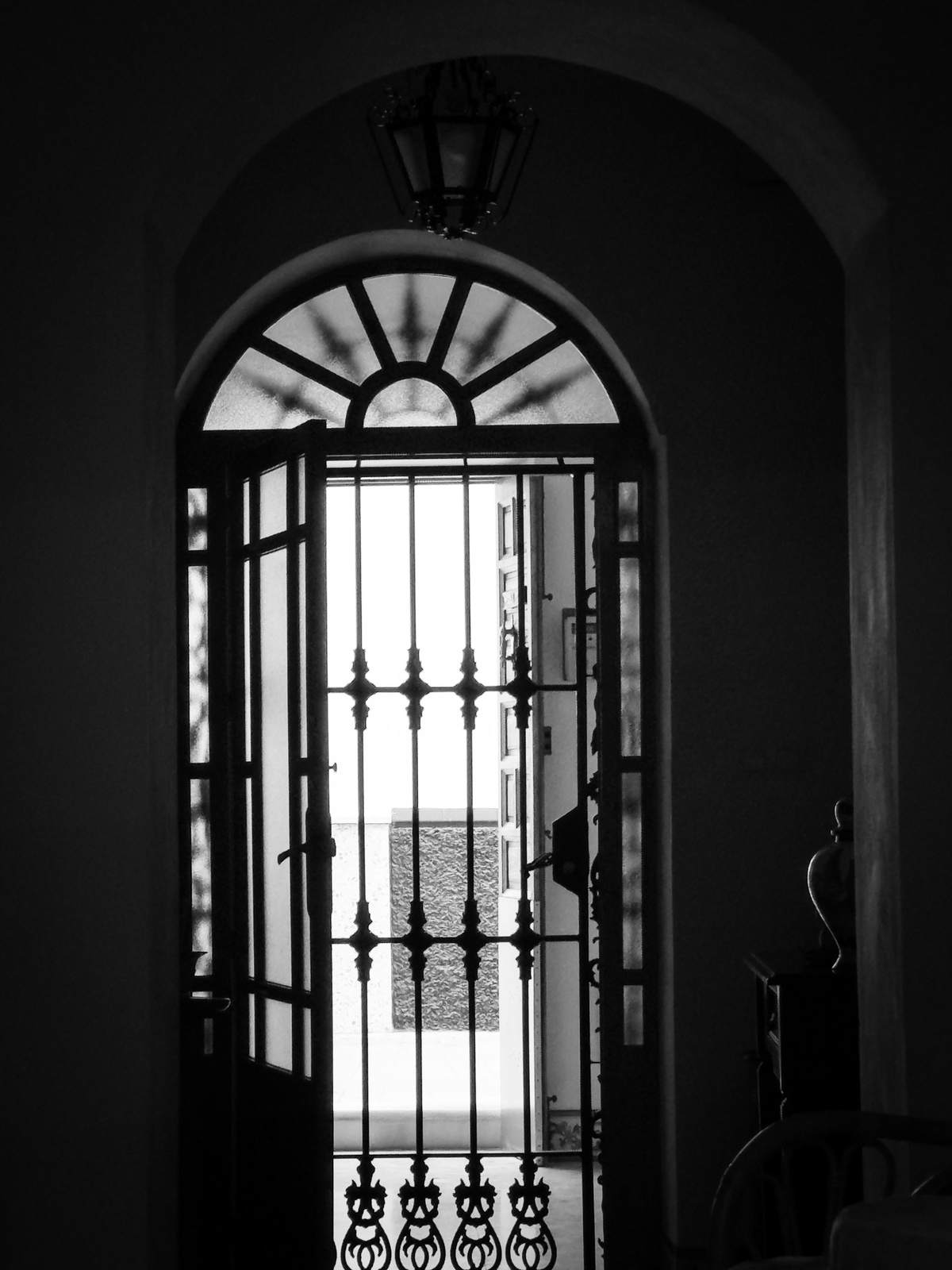Portón arqueado de hierro forjado en blanco y negro con la luz entrando desde el patio