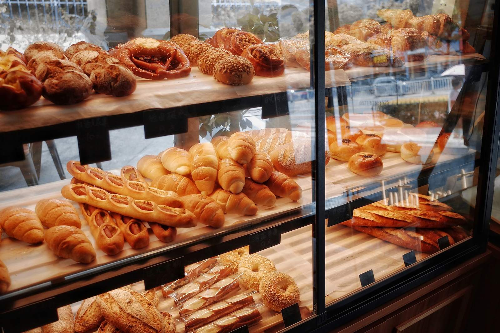 Vitrina de panadería con marcos de acero negro y bandejas de panes y medialunas