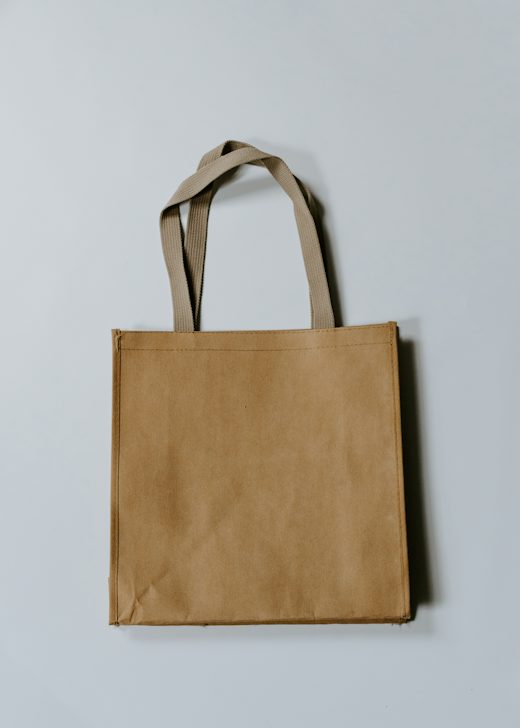 Bolso cuadrado de lona color arena con asas largas sobre un fondo azul grisáceo