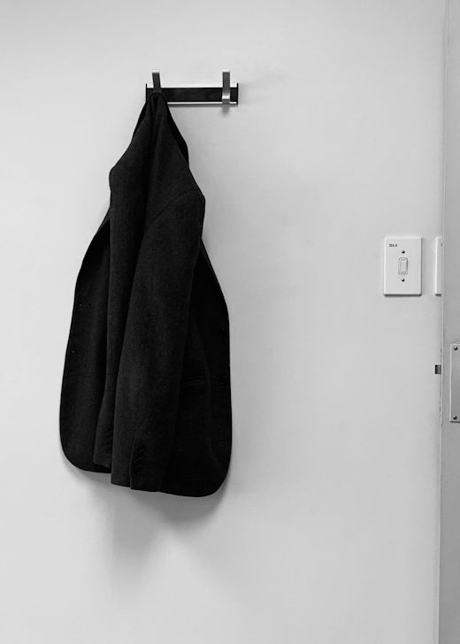 Chaqueta negra de lana colgada de un gancho en una pared blanca