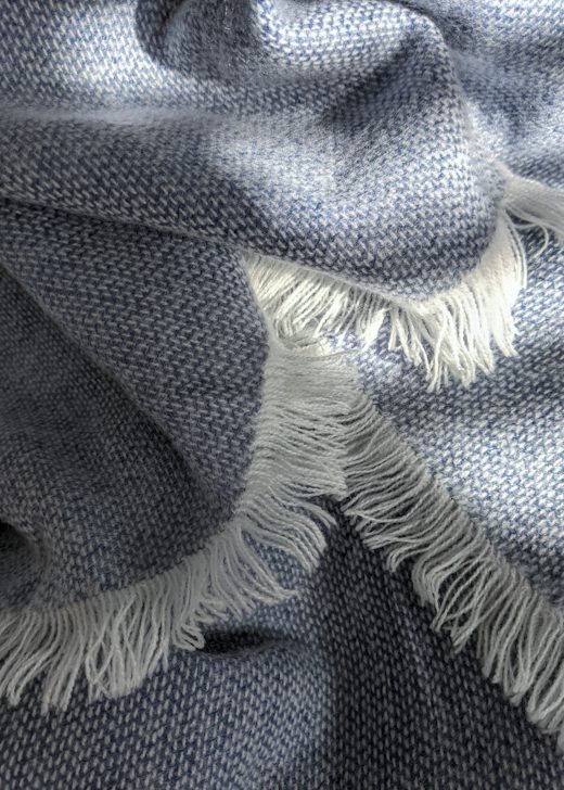 Detalle de una manta de lana gris azulada con flecos