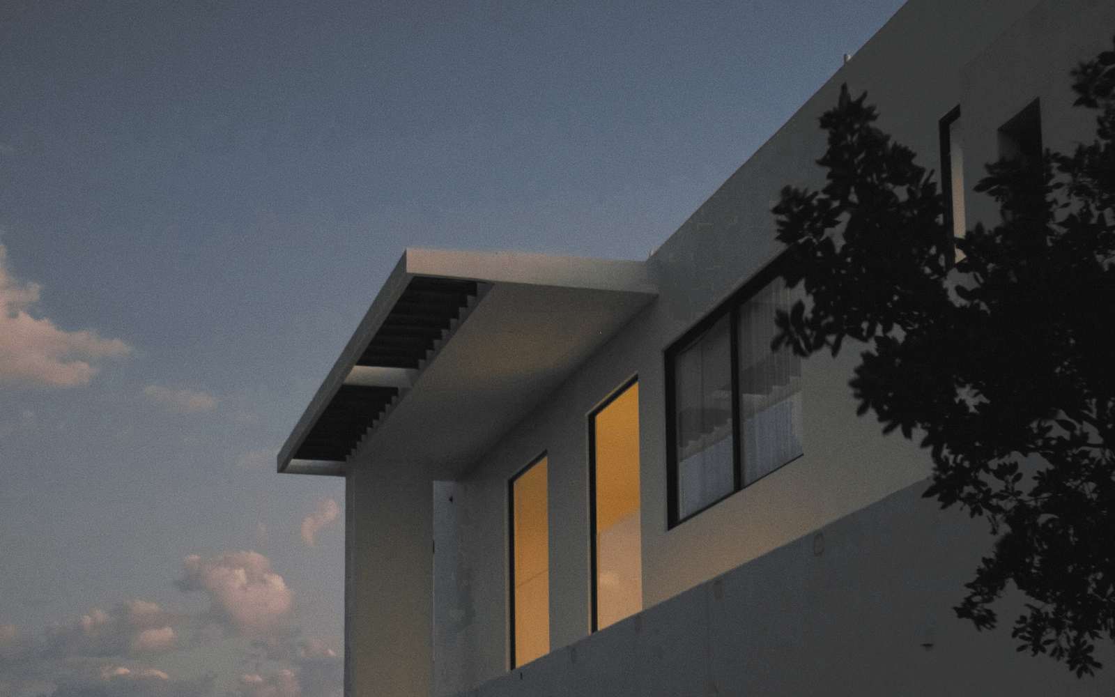 Casa blanca con alero y ventanas encendidas al anochecer