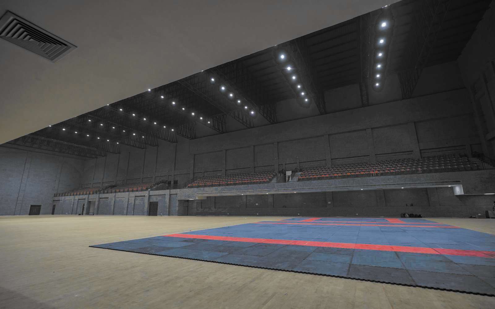 Interior de un pabellón deportivo con graderías rojas y piso de madera