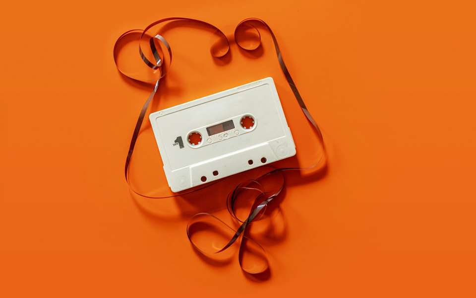 Un casete blanco con su cinta desenrollada sobre un fondo naranja