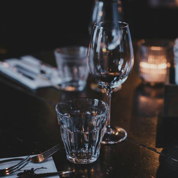 Copa de vino y vasos vacíos sobre una mesa oscura, con cubiertos y una vela desenfocada