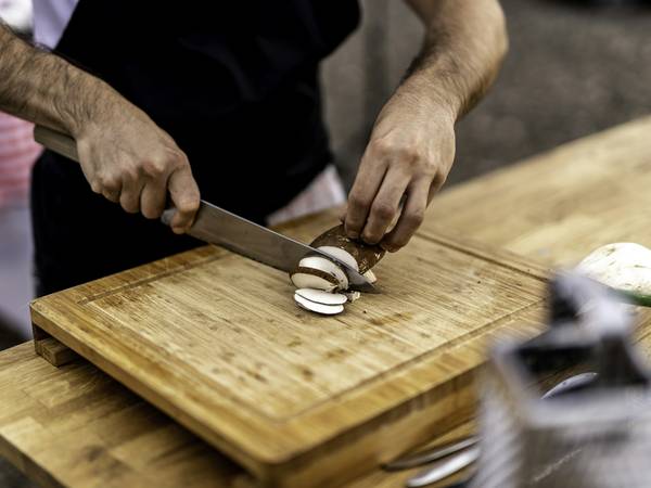 Manos cortando champiñones sobre una tabla de madera