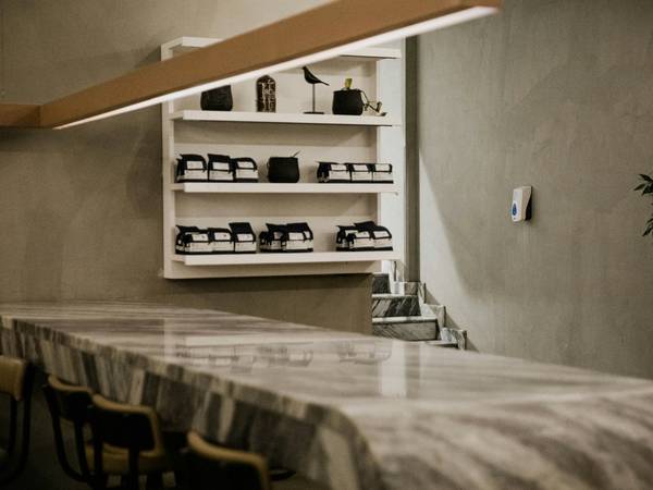 Mesón de mármol con estantes de tazas en un café de muros grises