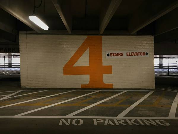 Muro de hormigón con un gran número 4 naranja y señales de escalera y ascensor, dentro de un estacionamiento