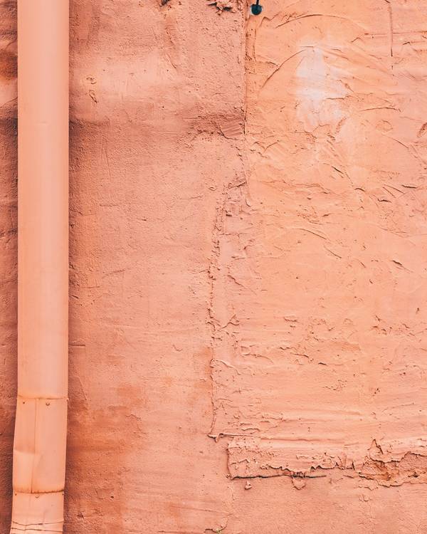 Muro rosado con un bajante de agua y textura de revoque