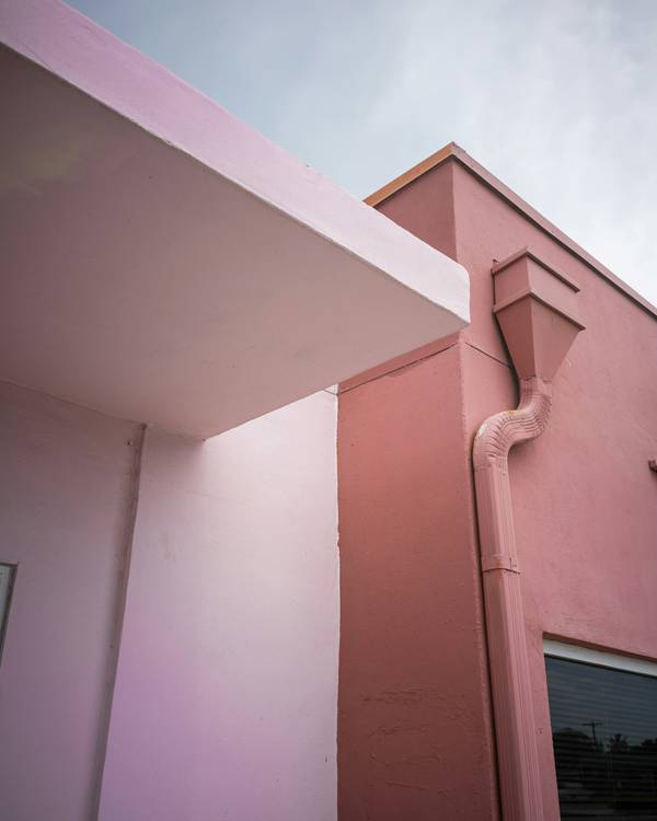 Edificio rosado con un alero y un bajante contra un cielo nublado