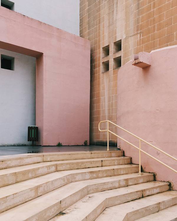 Escalera ancha de hormigón con barandas doradas junto a muros rosados y de ladrillo